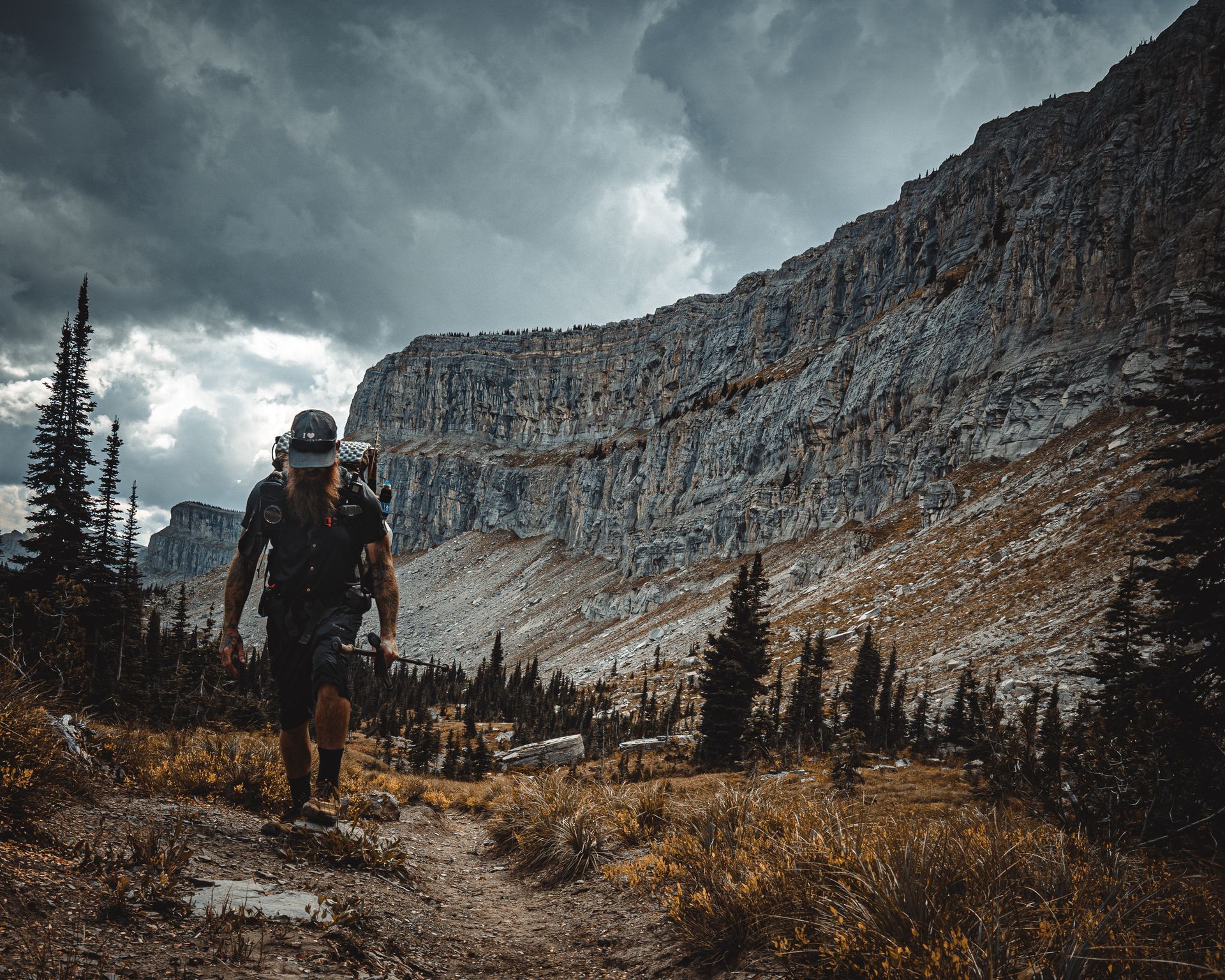 A man with a backpack is walking down a trail in the mountains.