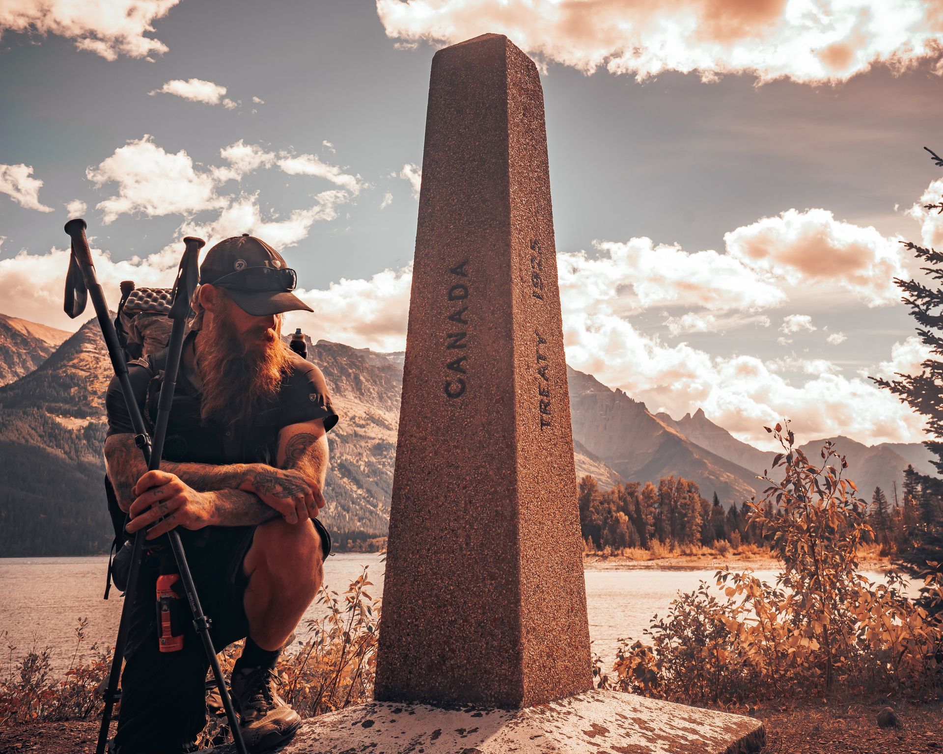 A man with a backpack is kneeling next to a stone that says canada on it.