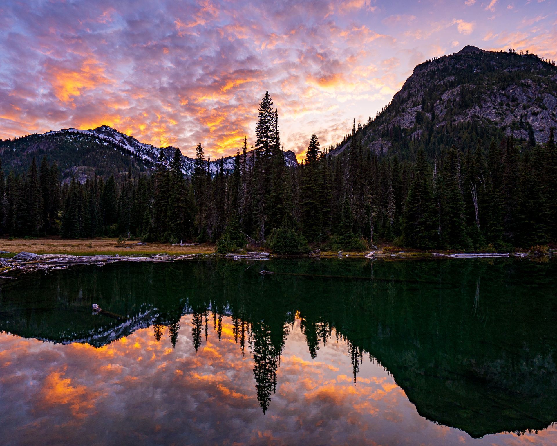 A lake surrounded by mountains and trees at sunset