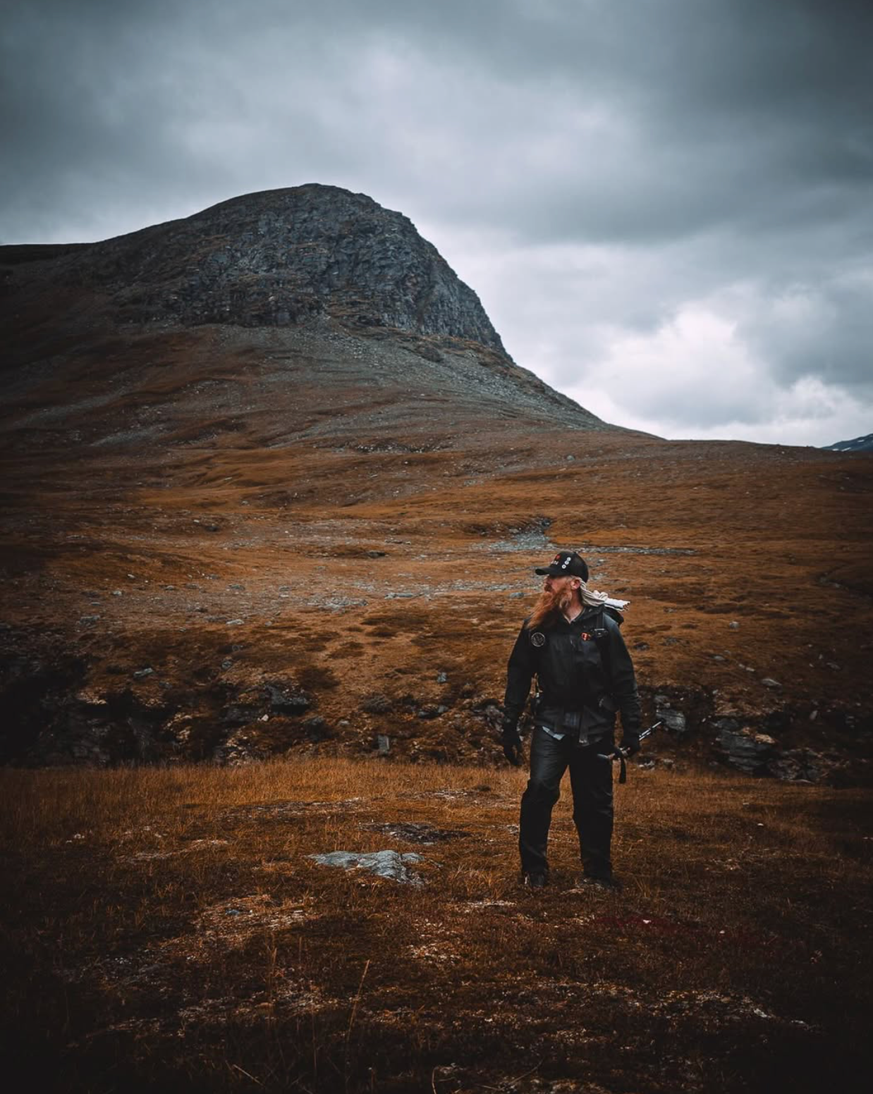 A man is standing in a field with a mountain in the background.