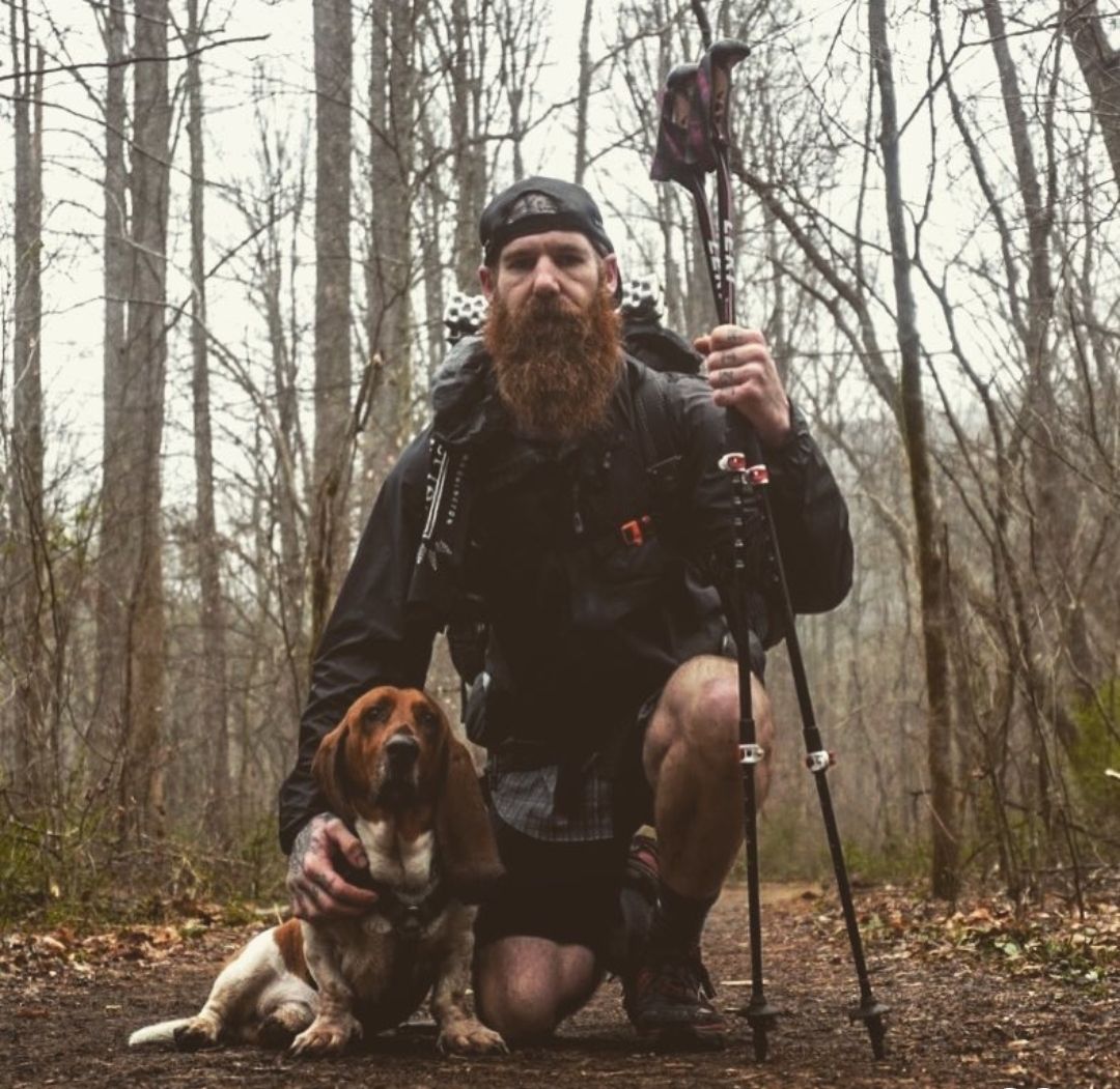 A man with a beard is kneeling down next to a dog