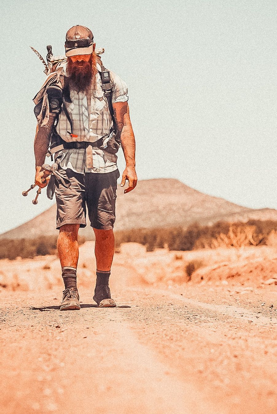 A man with a backpack is walking down a dirt road.