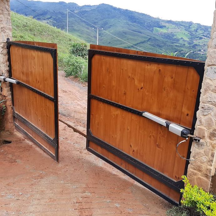 Puerta de madera abierta en un camino de tierra con montañas verdes al fondo.