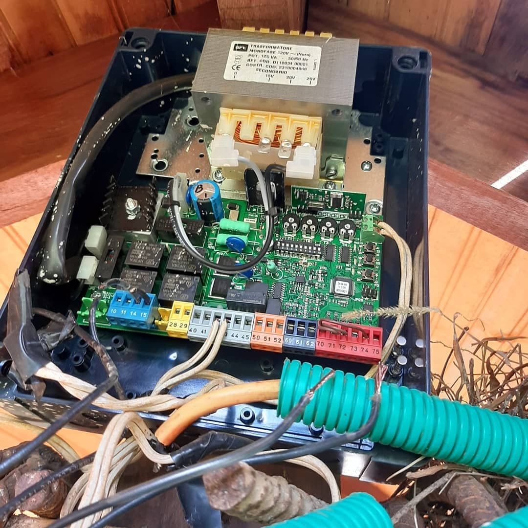 Dispositivo electrónico abierto con placas de circuito, cables y un transformador metálico dentro de una carcasa de plástico negro.