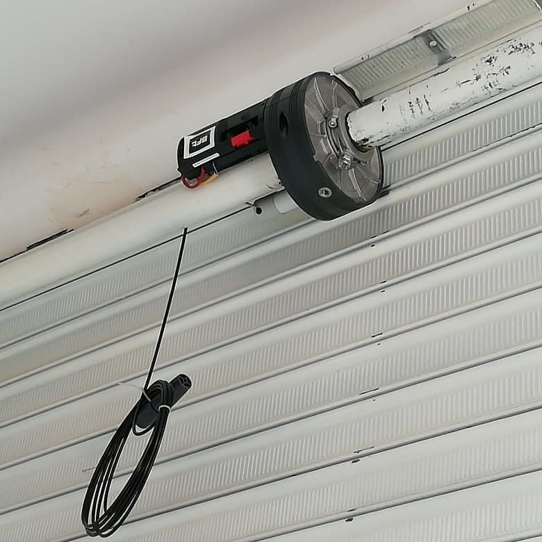 Cable negro enrollado colgando de un abrepuertas de garaje motorizado en un techo blanco.