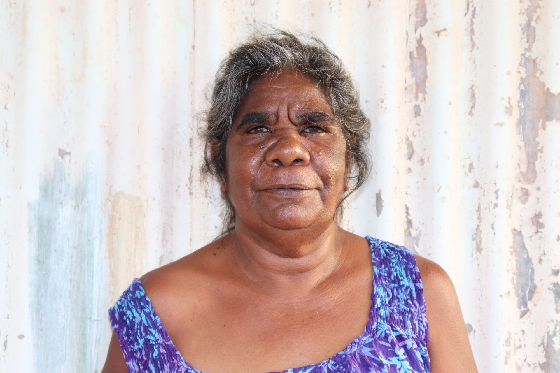 A woman in a purple top is standing in front of a white wall.