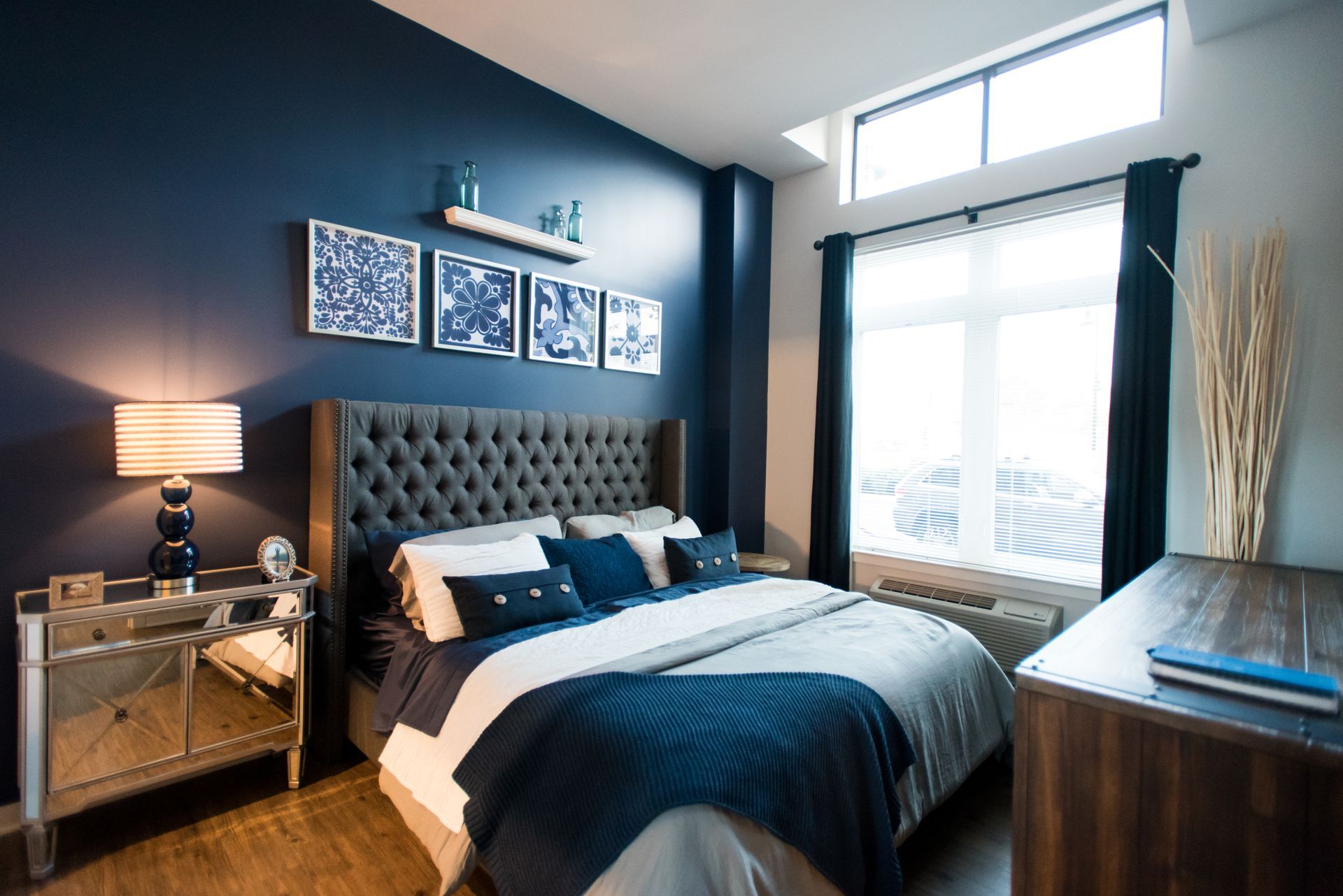 A bedroom with blue walls , a bed , a nightstand , and a window.