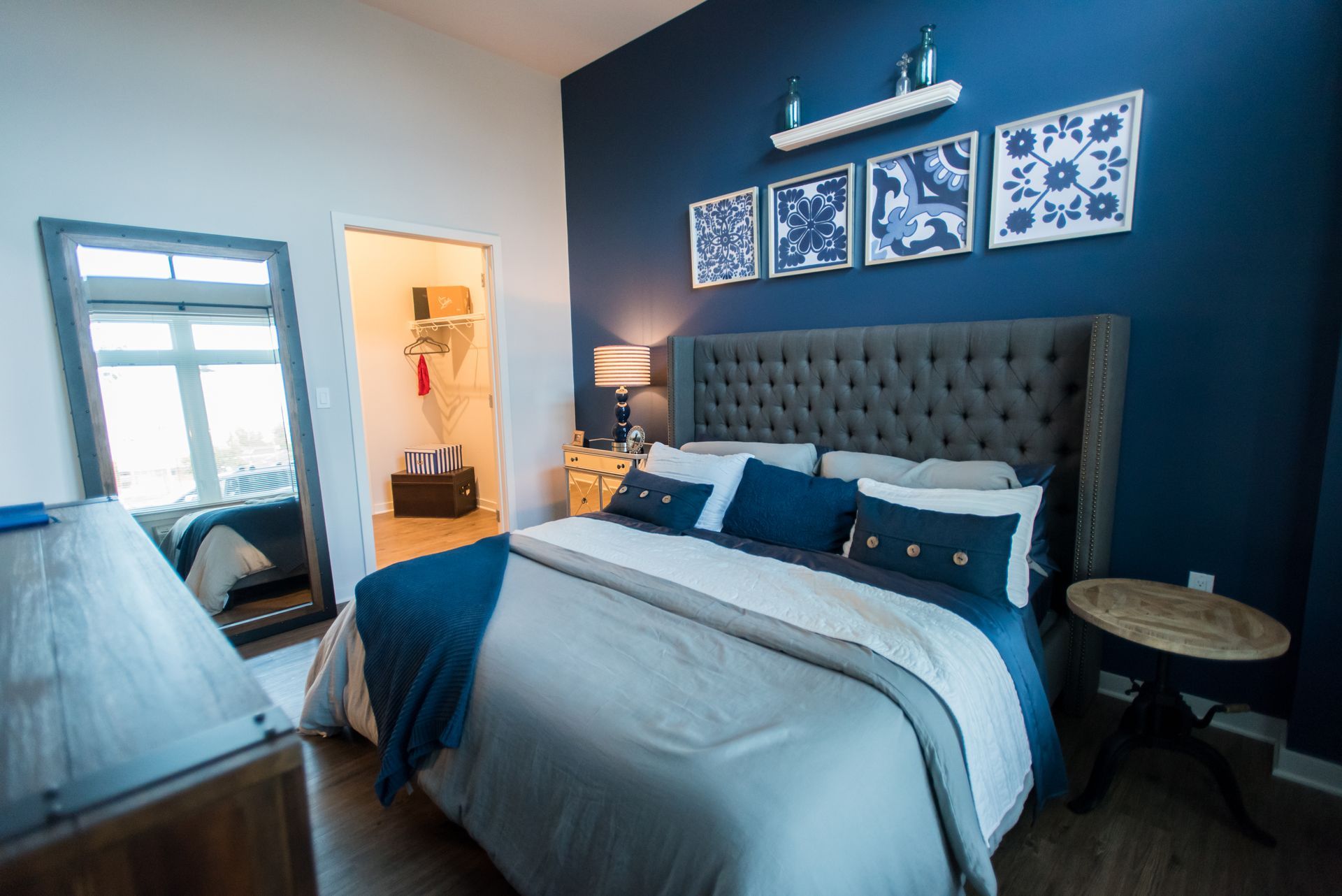 A bedroom with a bed , mirror , nightstand , and blue walls.