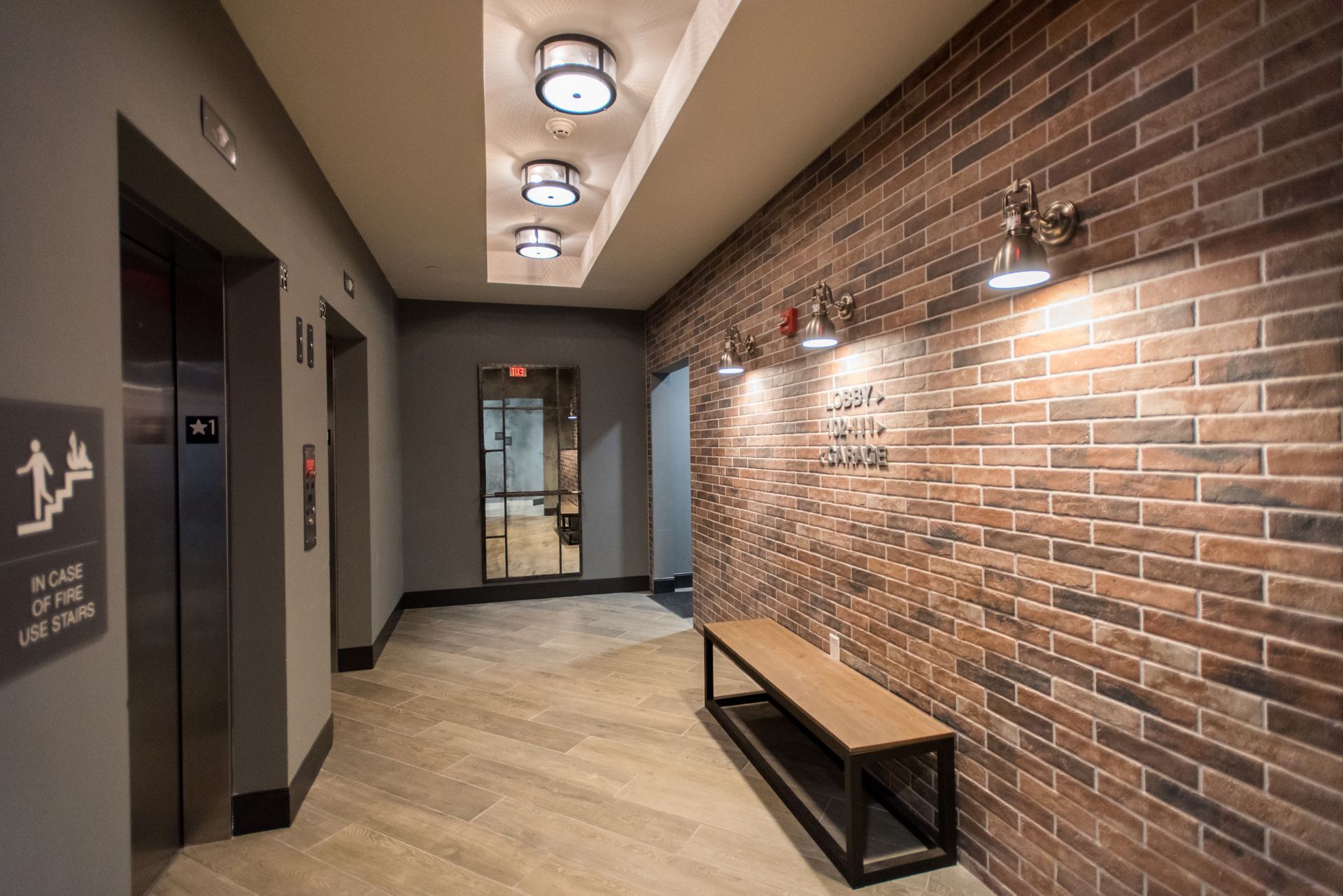A hallway with a brick wall and an elevator.