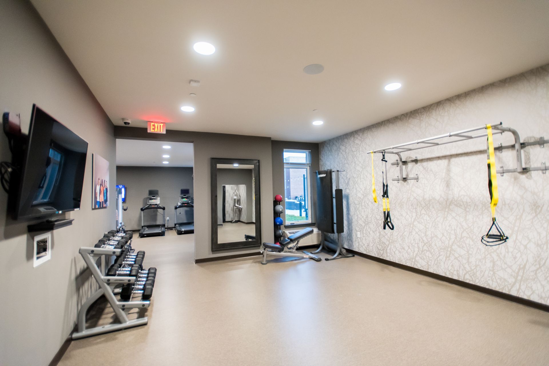 A gym with a treadmill , dumbbells , and a television.