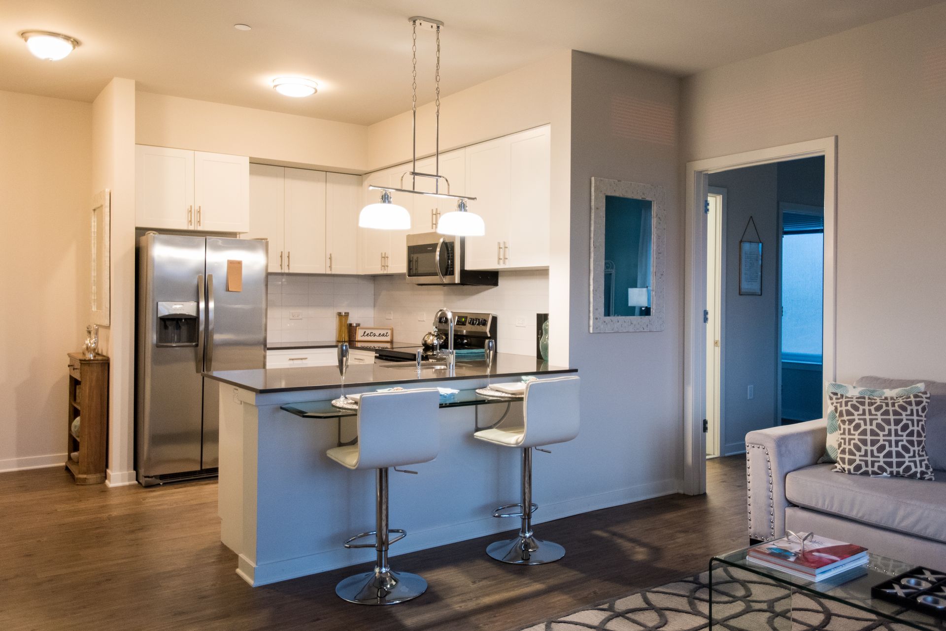 A living room with a couch and a kitchen with a stainless steel refrigerator.