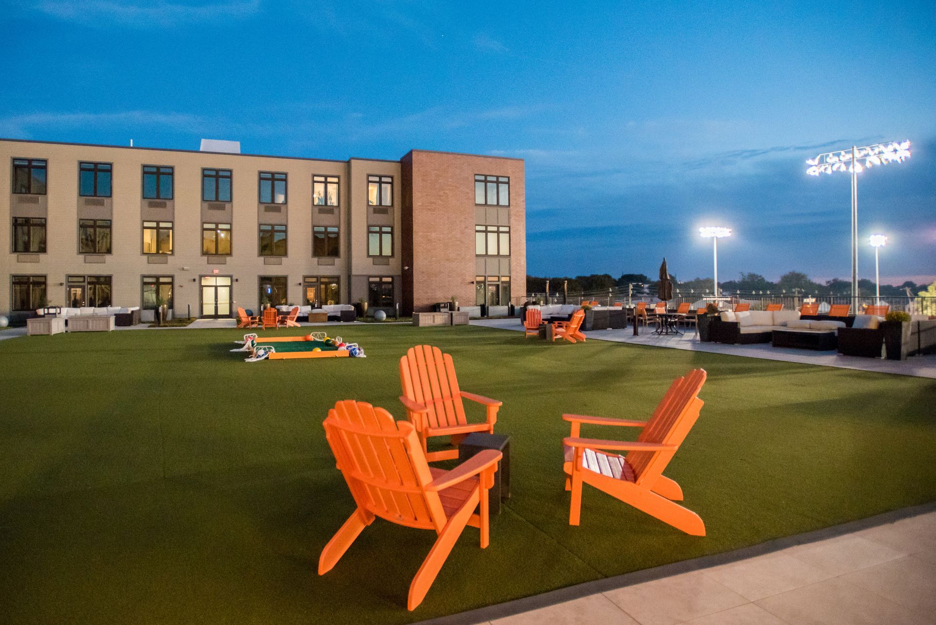 Two orange lawn chairs are sitting on a lush green lawn in front of a large building.