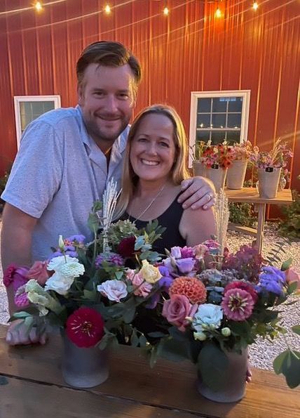 A man and a woman are standing next to a table with vases of flowers.