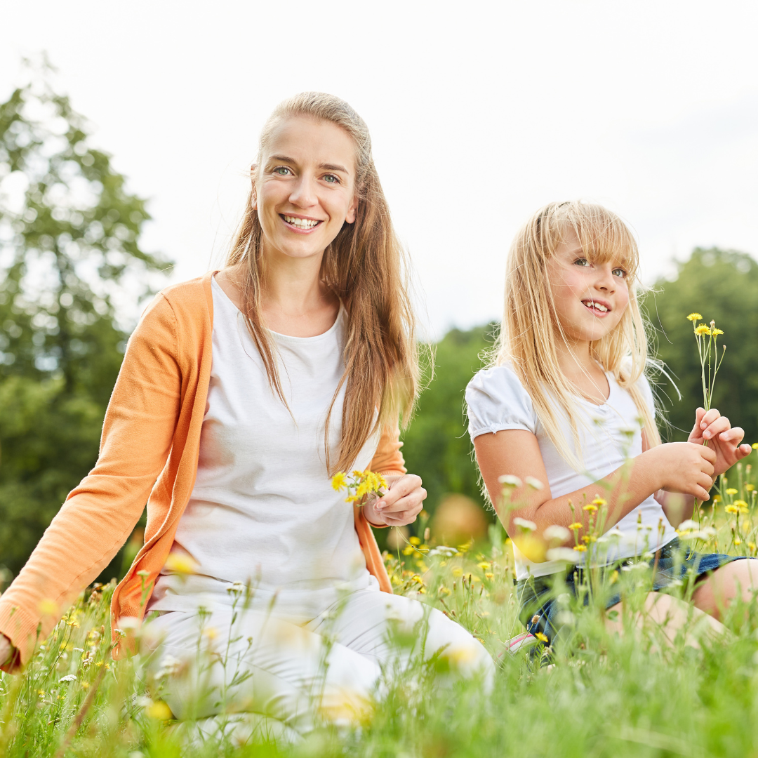 A woman and a little girl are sitting in a field of flowers.