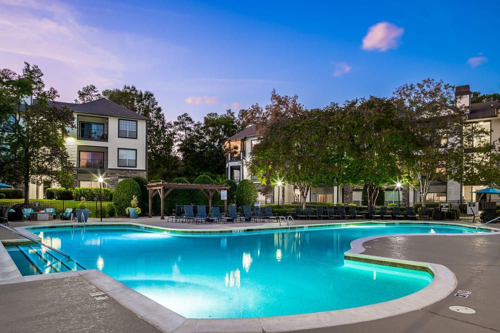 a large swimming pool is lit up at night in front of a building at Marquis Carmel Commons in Charlotte, NC.