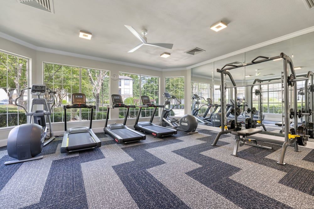 a large gym with treadmills, exercise bikes, and a ceiling fan at Marquis  Carmel Commons in Charlotte, NC.