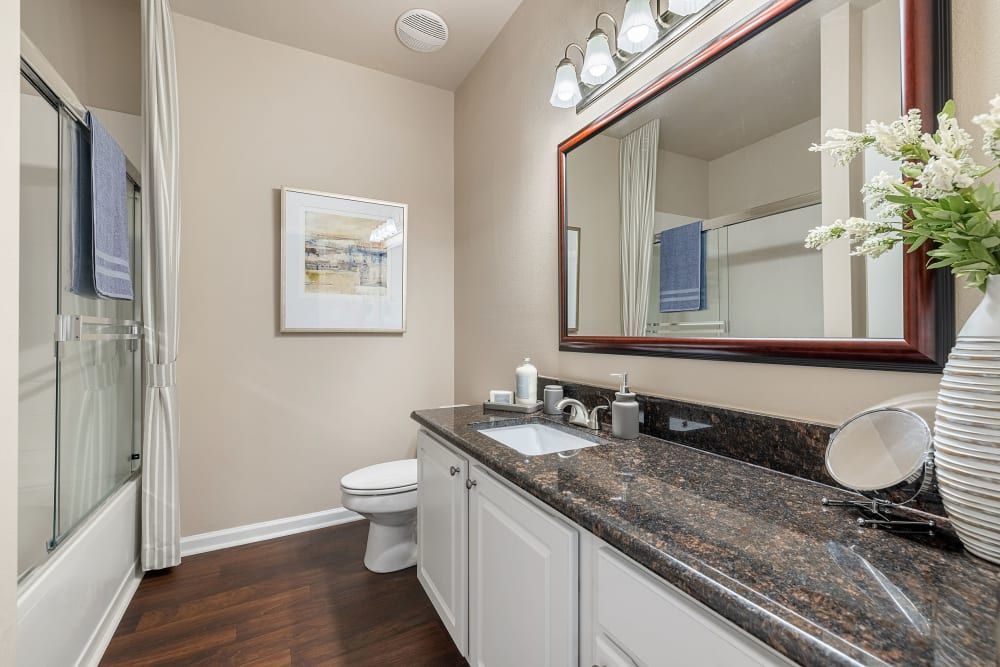 a bathroom with a toilet, sink, mirror, and shower at Marquis Carmel Commons in Charlotte, NC.