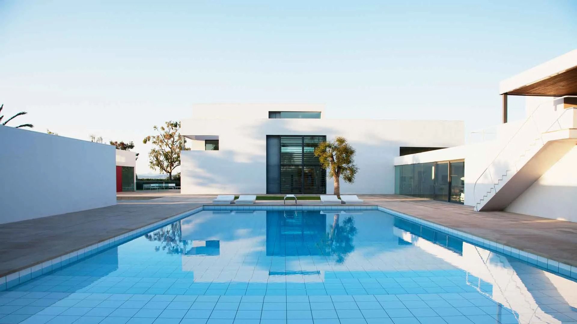 Modern white house with a blue swimming pool reflecting the sky.