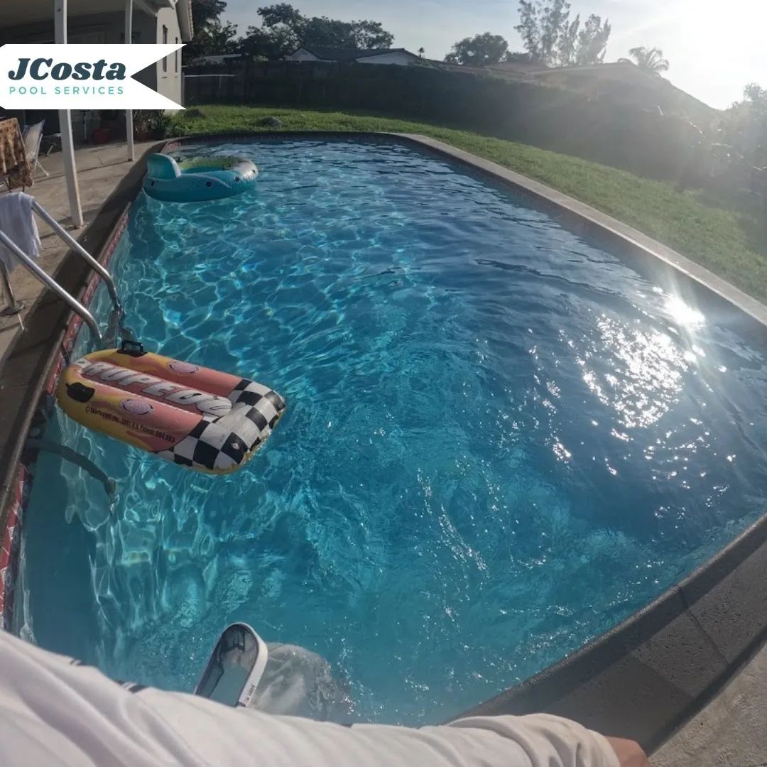 Pool with blue water, inflatable raft, and person's leg entering. Sunny outdoor setting.