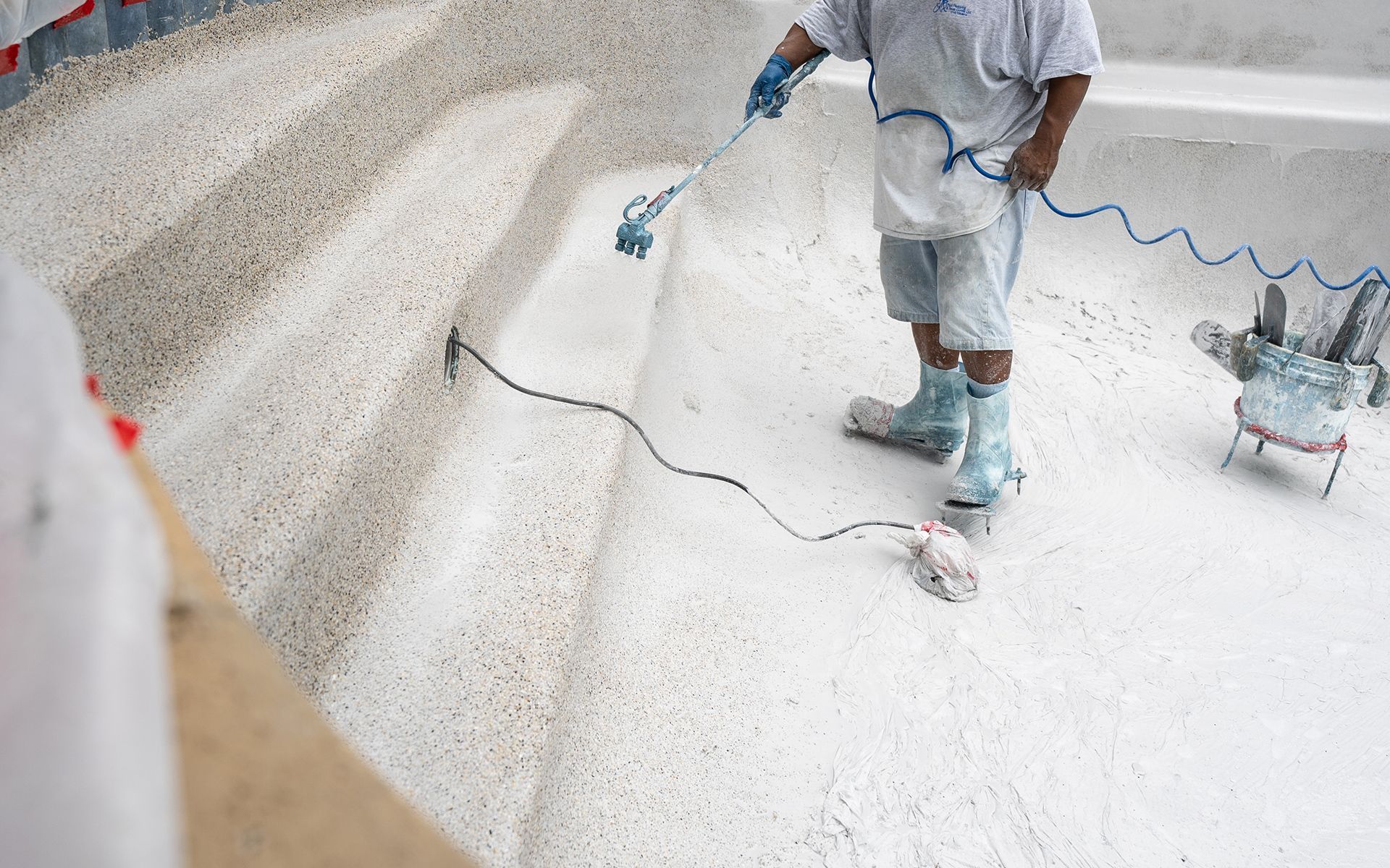 Person spraying white pool surface with equipment.