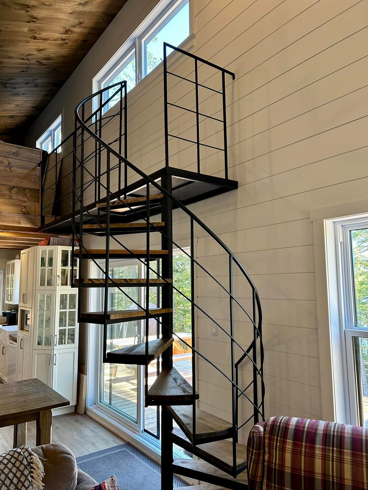 Escalier en colimaçon menant à une mezzanine dans une pièce haute, lambrissée et dotée de grandes fenêtres