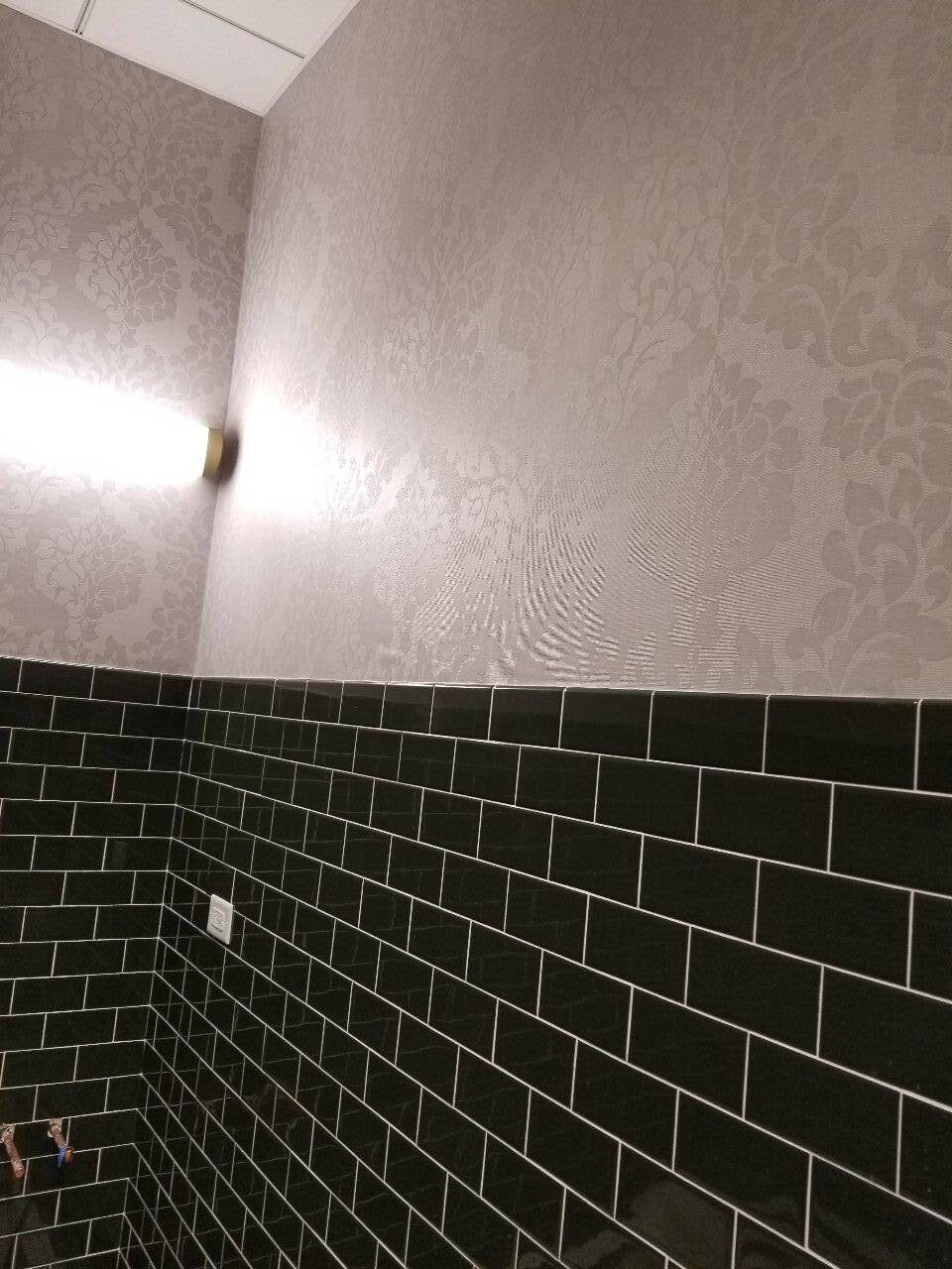 A bathroom with black tiles and a light on the wall.