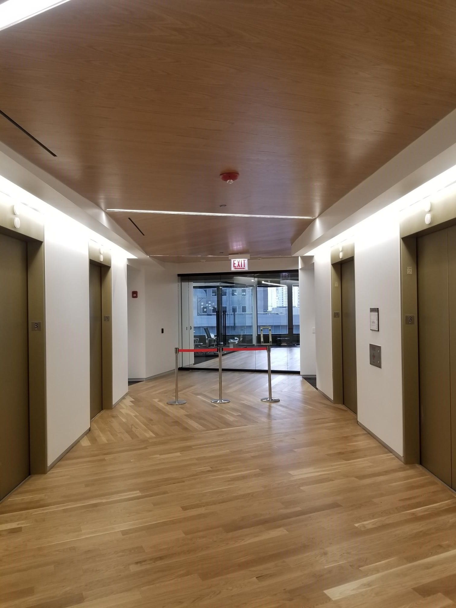 A long hallway with wooden floors and elevators in a building.
