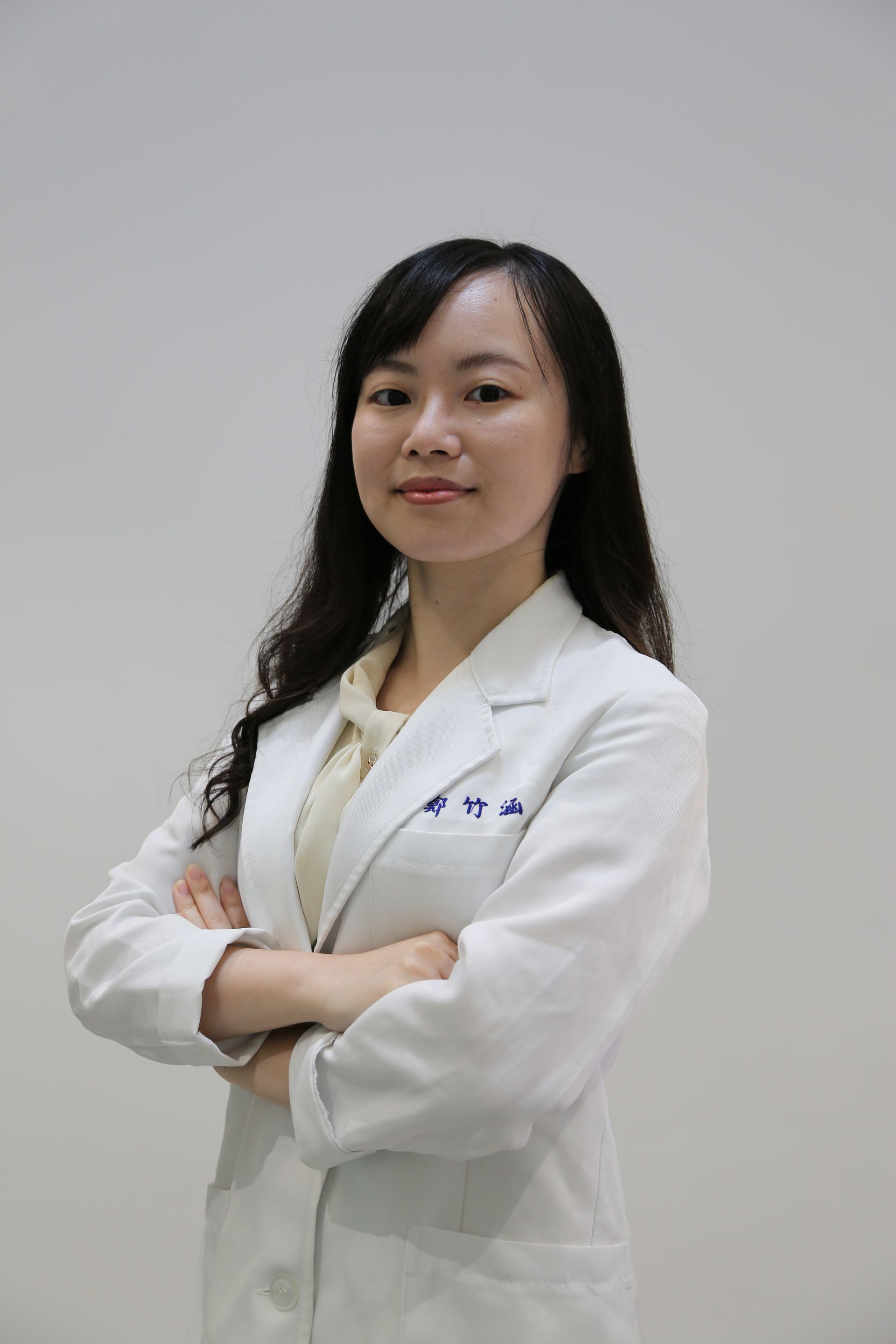 一位身穿白色實驗服的女士,雙手交叉,看著相機。背景為灰色。