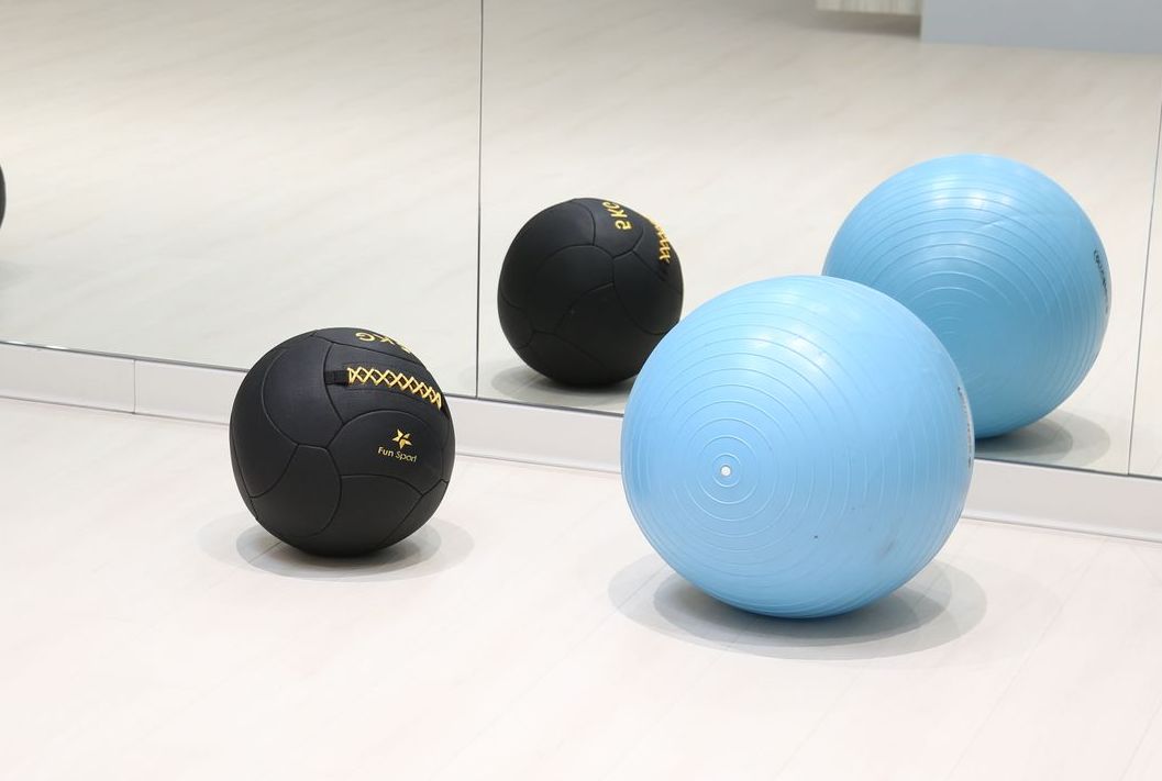兩個黑色和兩個藍色的健身球放在淺色地板上，其中一個黑色的球在鏡子中反射。