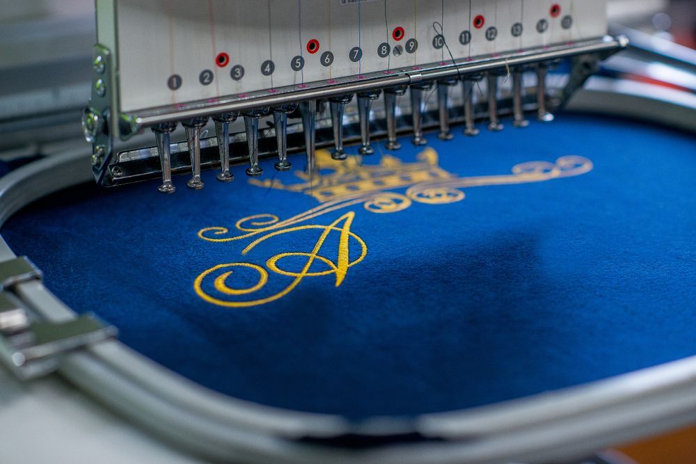 A Machine is Embroidery a Letter a on a Blue Cloth — Tableland Workwear In Tolga, QLD