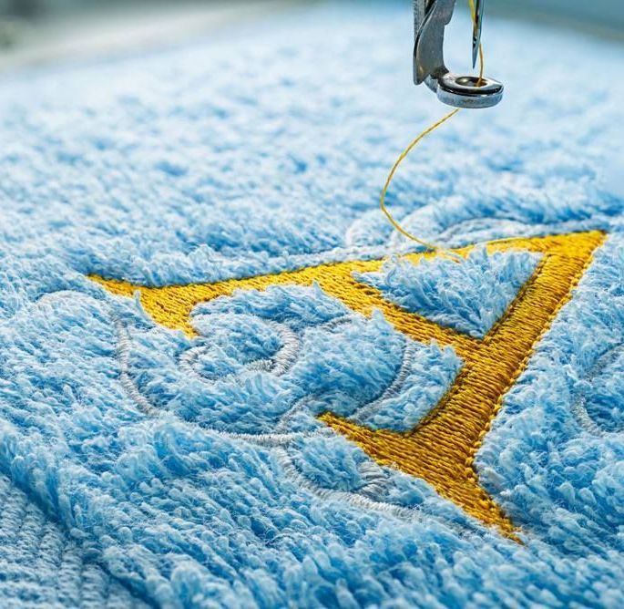 A Close Up Of A Sewing Machine Embroidery On A Blue Towel — Tableland Workwear In Tolga, QLD