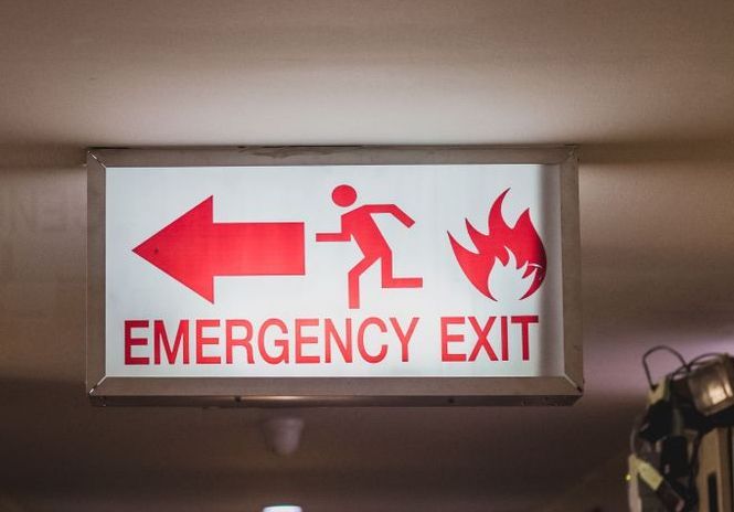 A Red and White Emergency Exit Sign With an Arrow Pointing to the Left — Tableland Workwear In Tolga, QLD