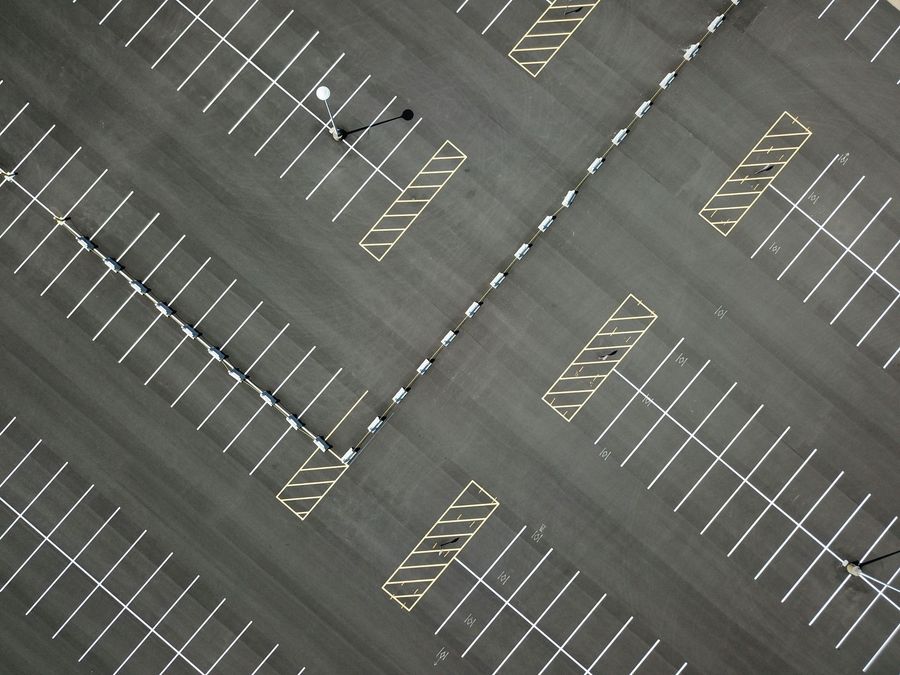A person uses a yellow roller to apply fresh, black asphalt sealant to a smooth driveway on a sunny day.