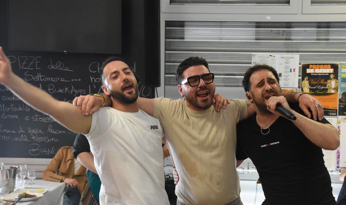 Tre uomini sono in piedi uno accanto all'altro e cantano nei microfoni.