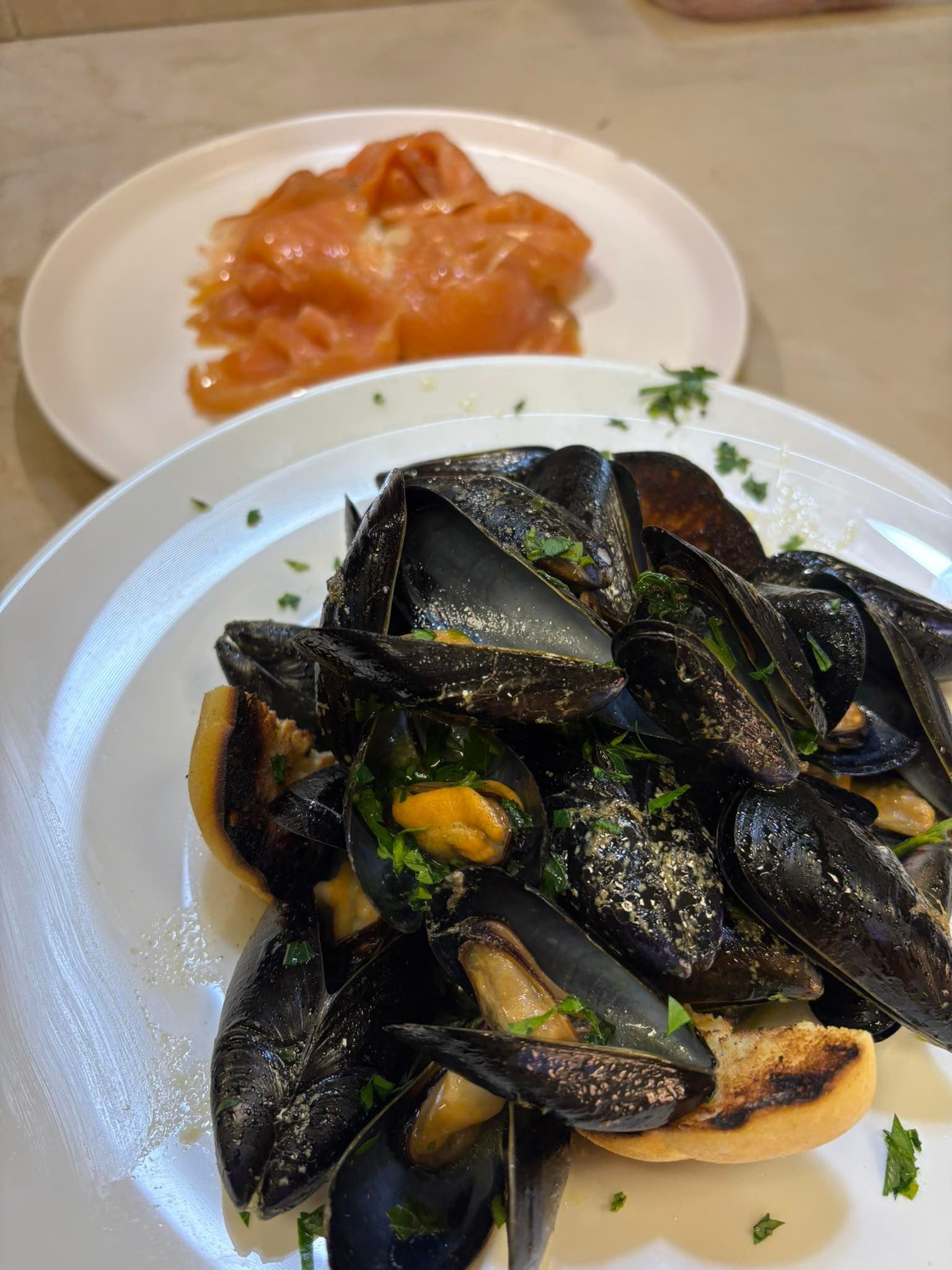 Su un tavolo ci sono un piatto di cozze e un piatto di salmone.