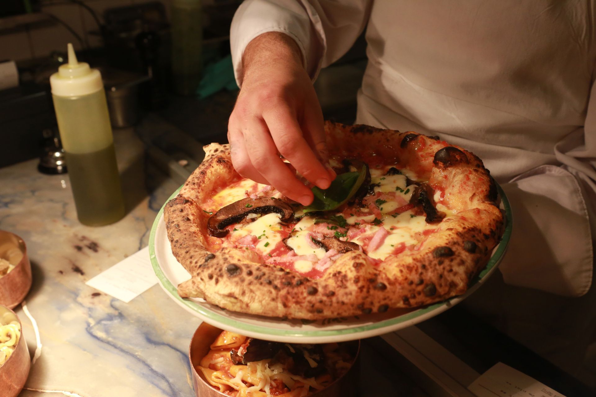 Una persona sta mettendo il basilico su una pizza messa su un piatto.