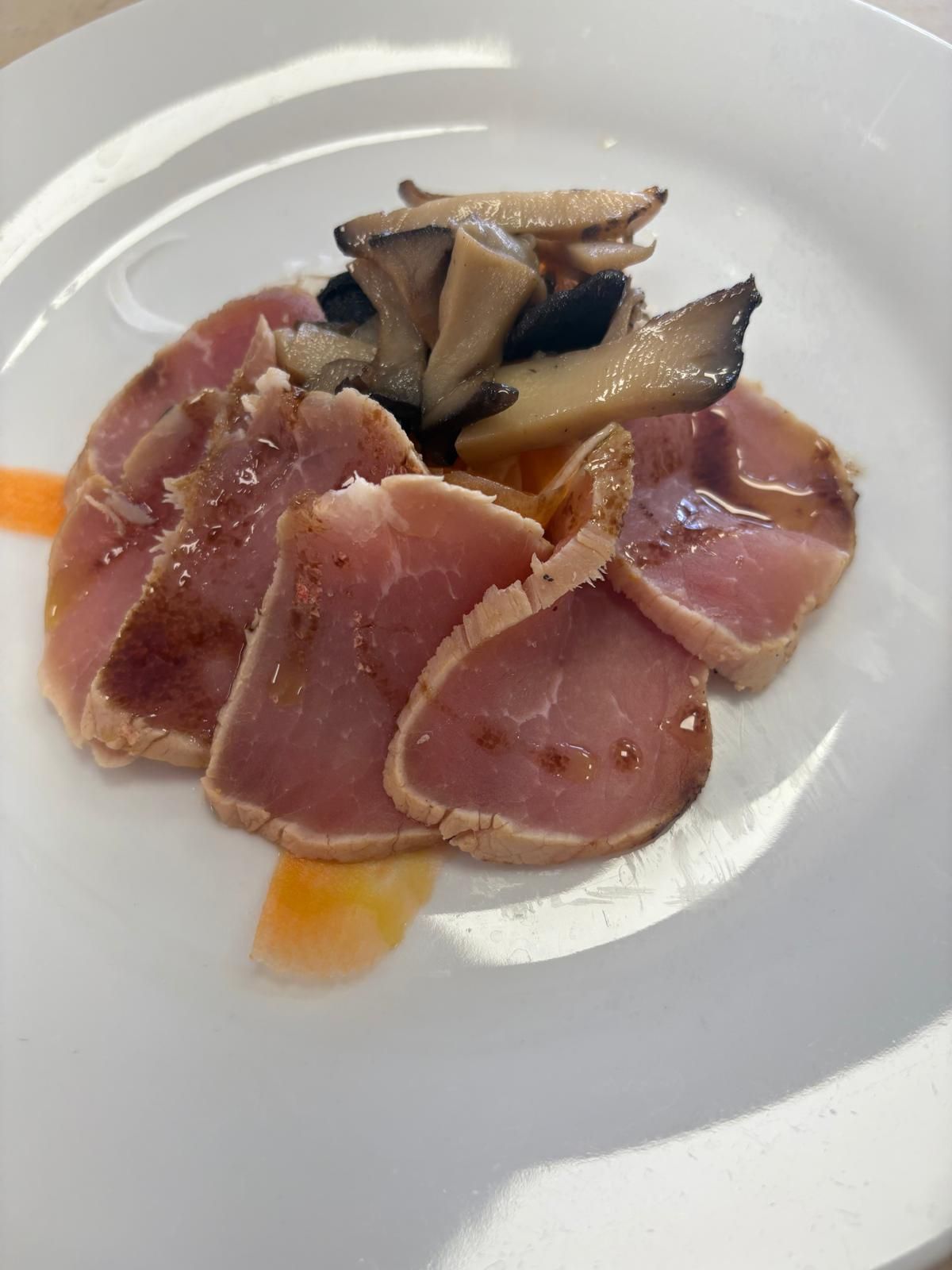 Un piatto bianco con sopra fette di carne e funghi