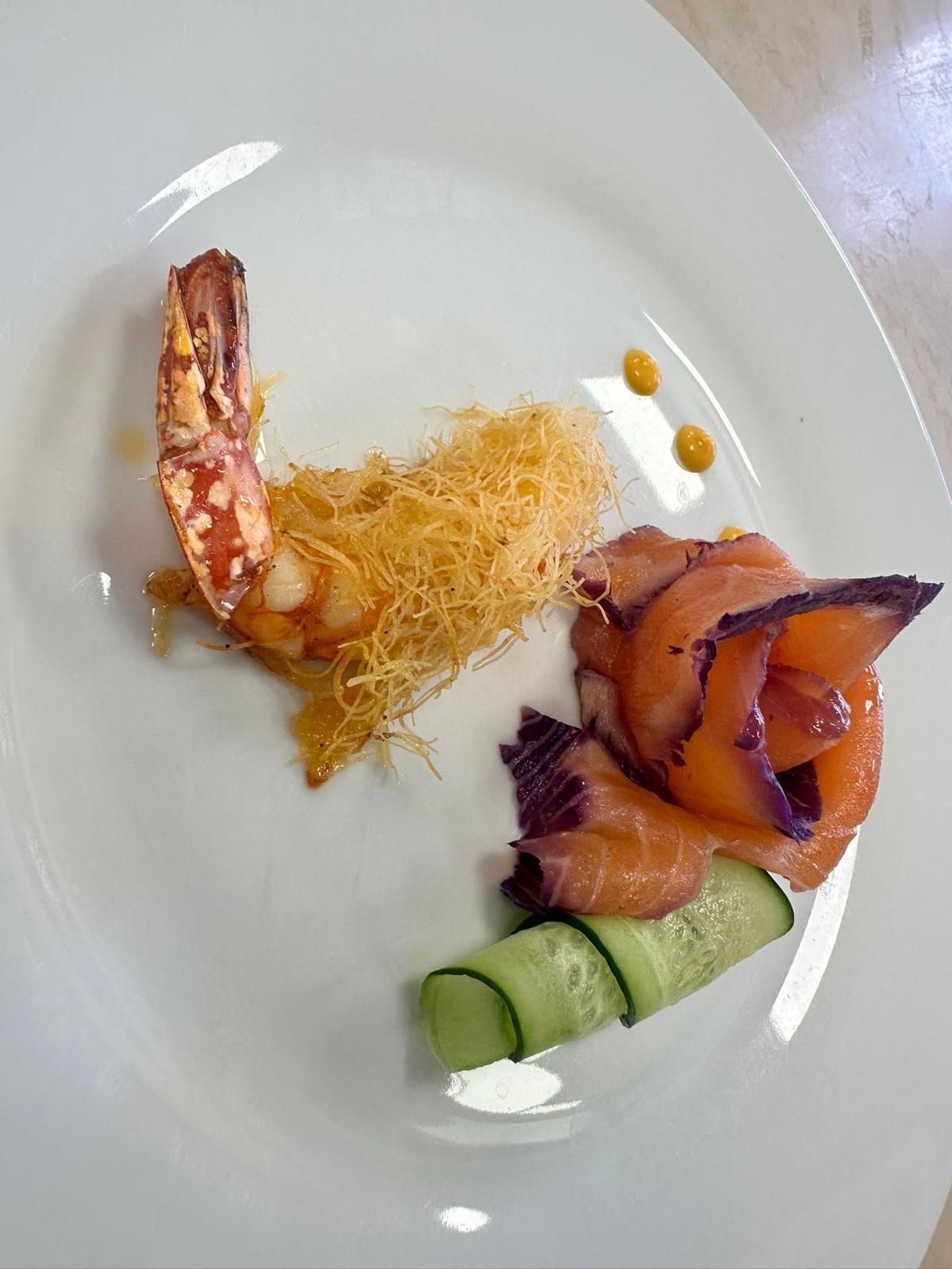 Un piatto bianco guarnito con gamberi, salmone affumicato e cetriolo.