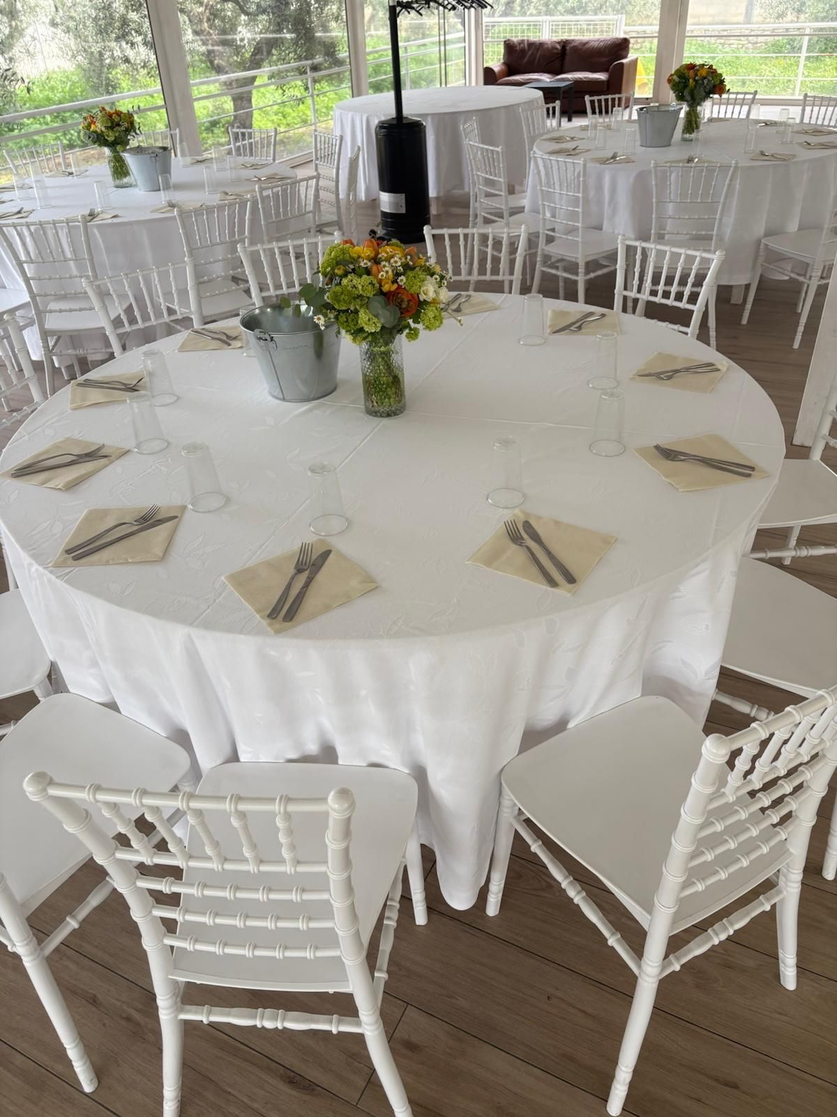 Per un ricevimento di nozze è allestito un tavolo rotondo con una tovaglia bianca e sedie bianche.