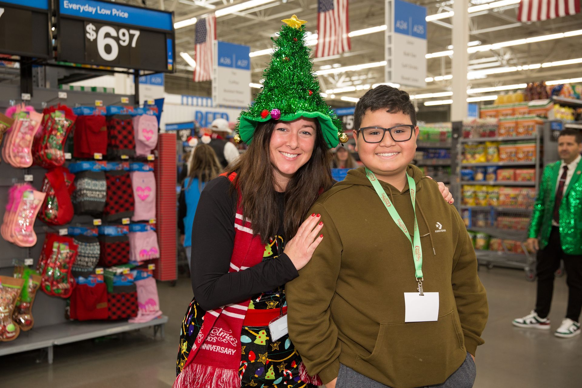 A boy and a girl are posing for a picture in a store . the girl is wearing a christmas tree hat.