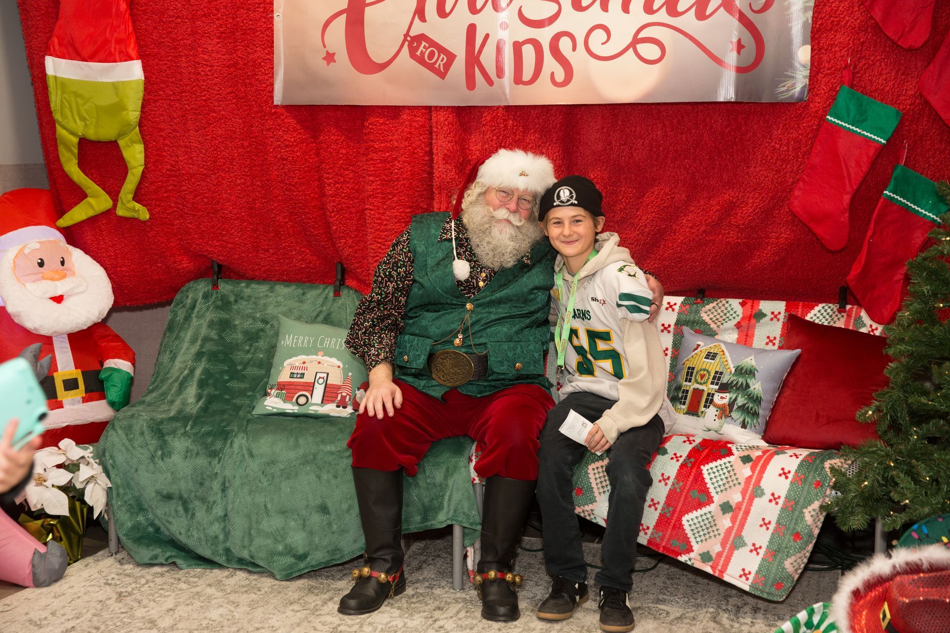 A boy is sitting next to santa claus on a couch.