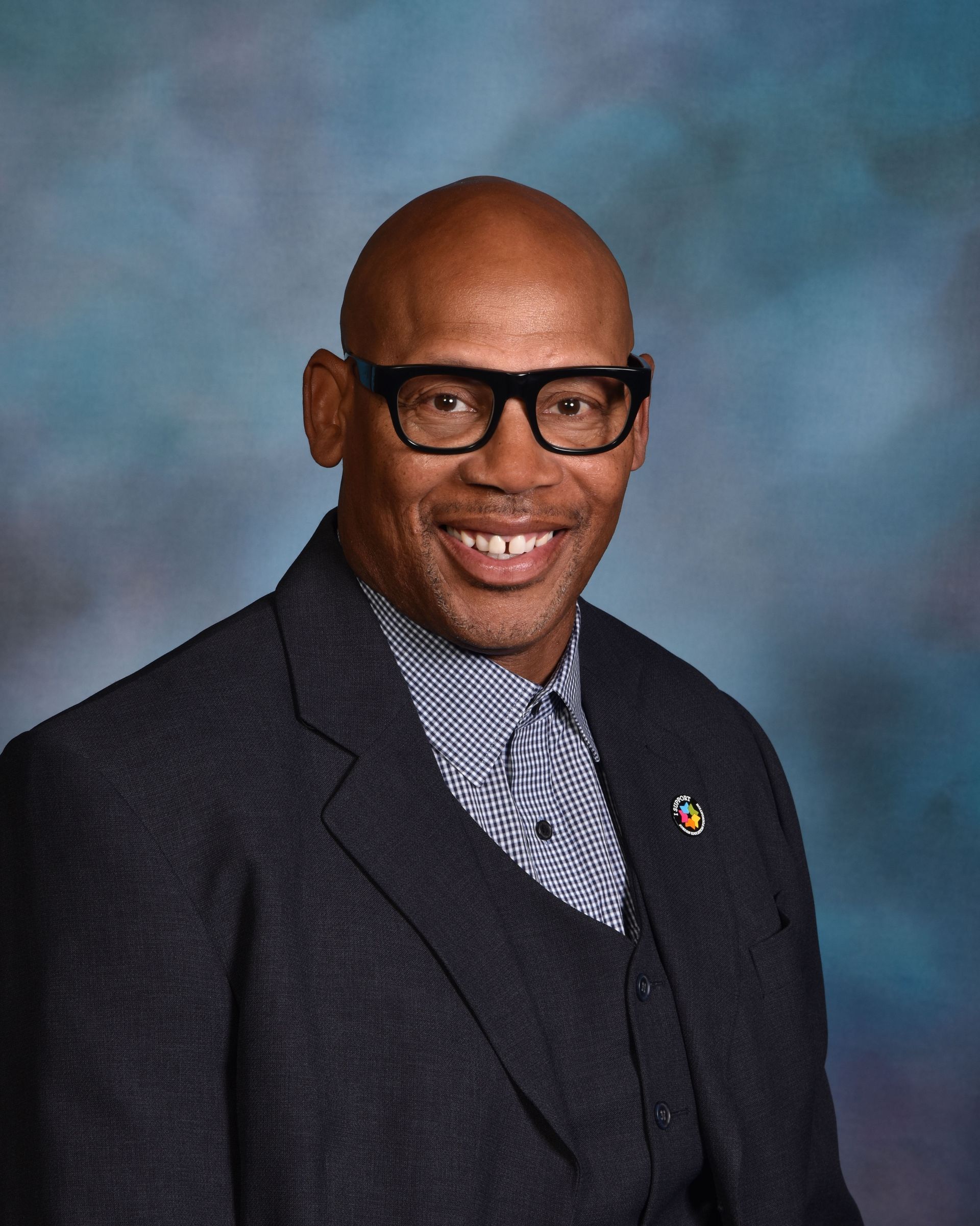 A bald man wearing glasses and a suit is smiling for the camera.