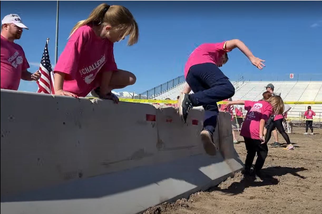 A girl in a pink shirt is jumping over a concrete barrier
