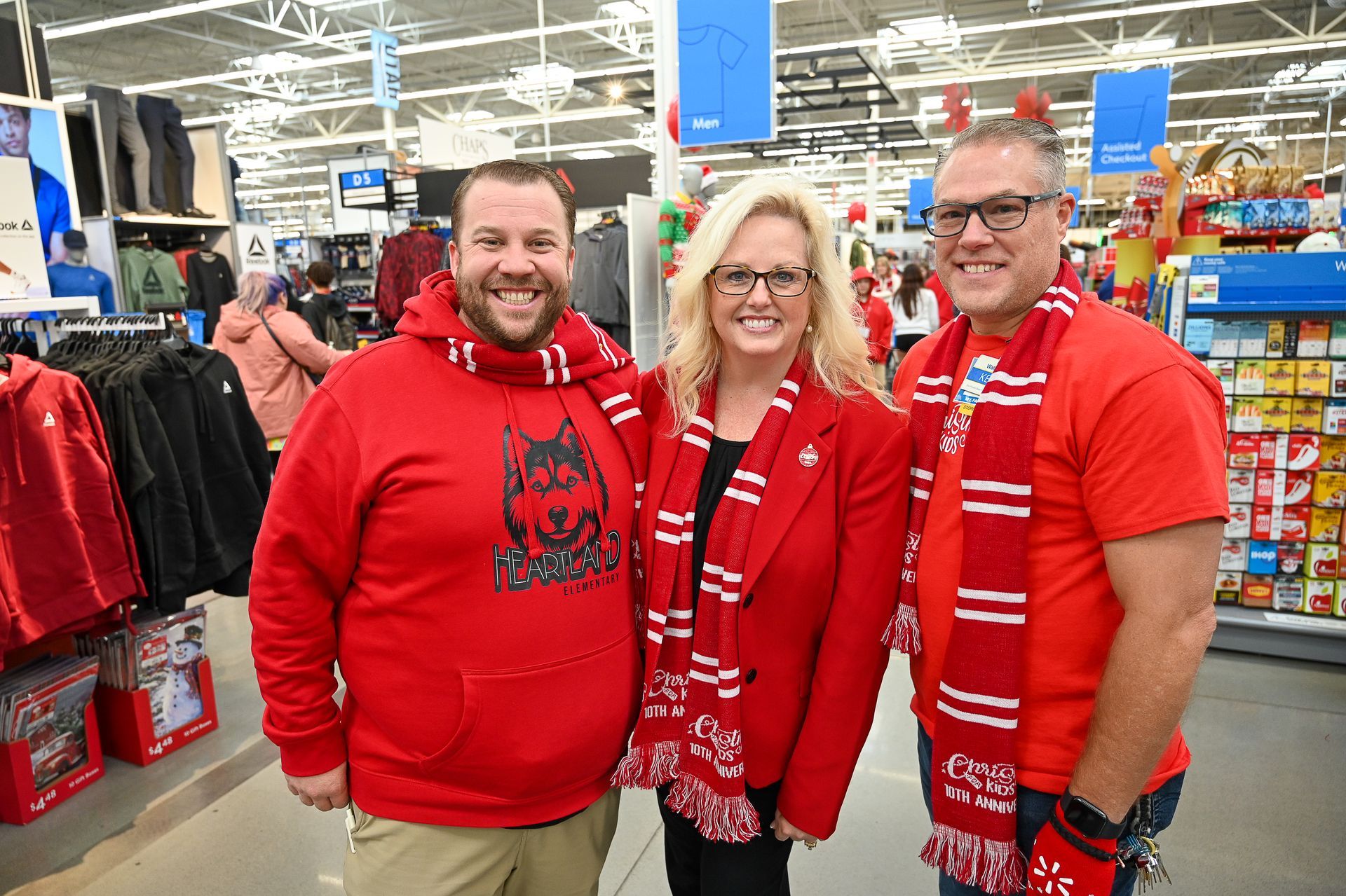 Three people wearing red shirts and scarves are posing for a picture in a store.