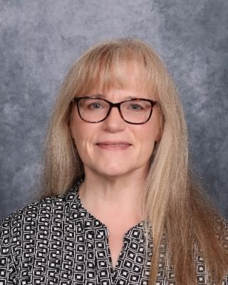 A woman wearing glasses and a red floral jacket is smiling for the camera.