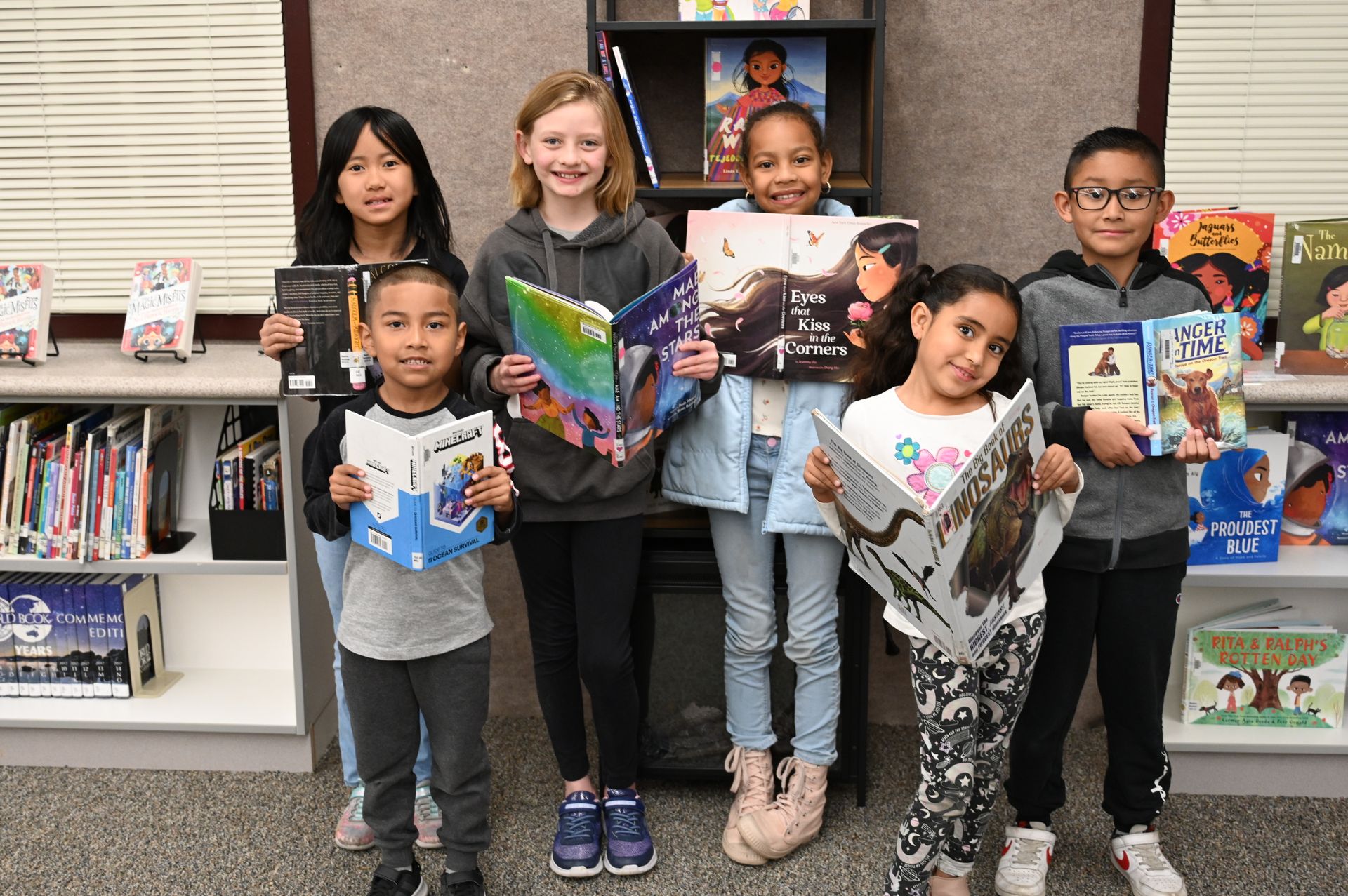 A group of children are holding books in a library.