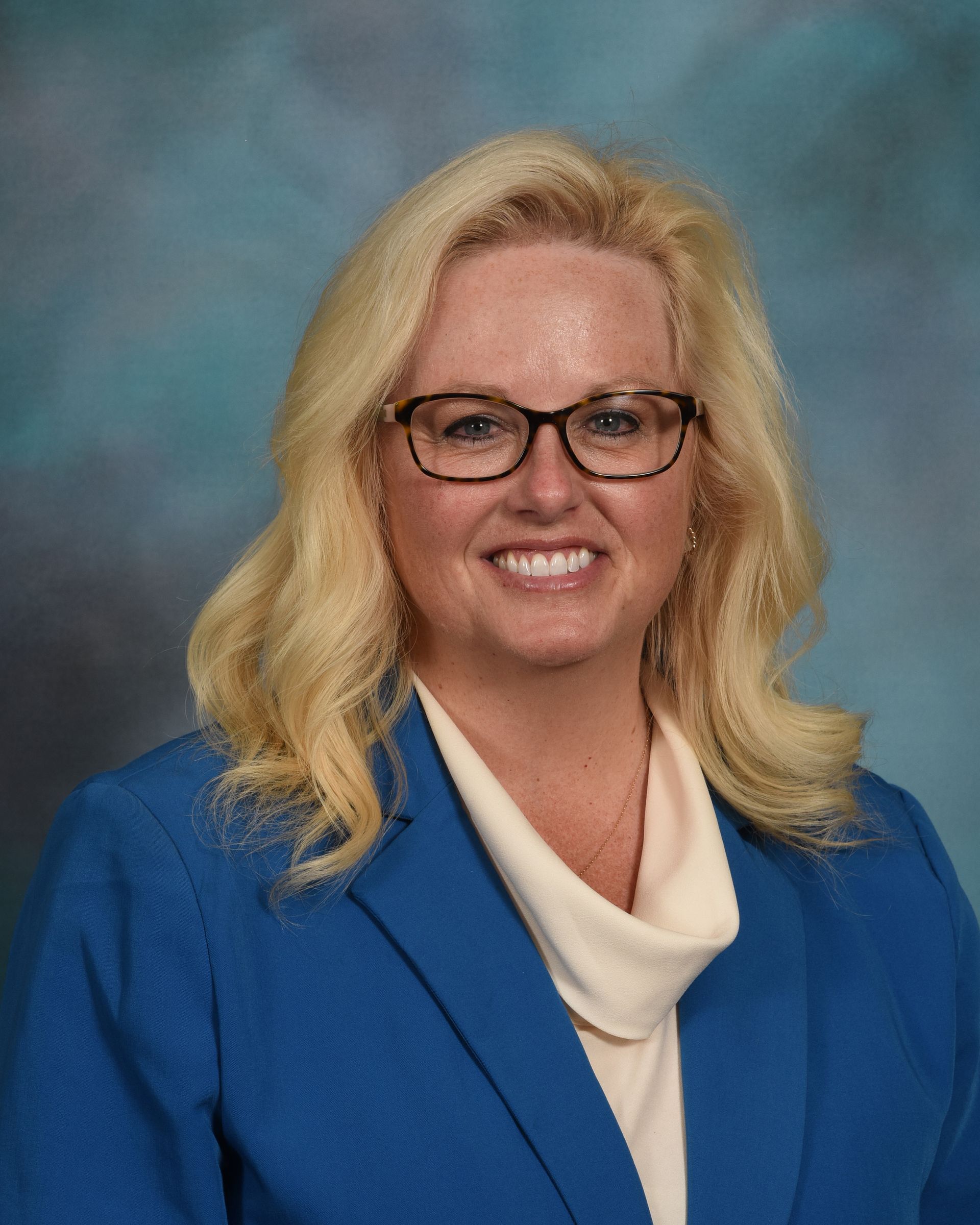 A woman wearing glasses and a blue jacket is smiling for the camera.