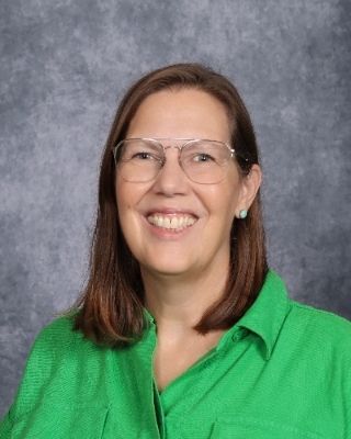 A woman wearing glasses and a blue jacket is smiling for the camera.
