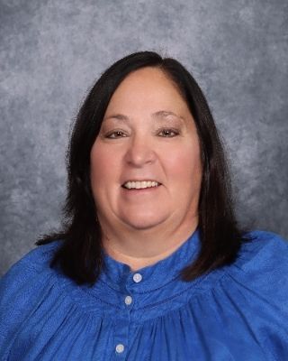 A woman in a blue jacket and black shirt is smiling for the camera.