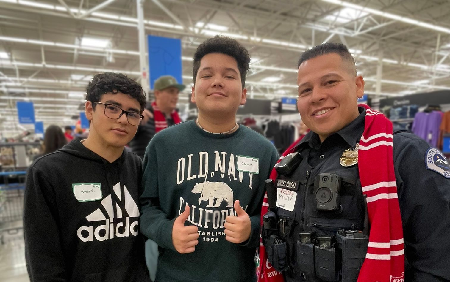Three young men are posing for a picture with a police officer in a store.